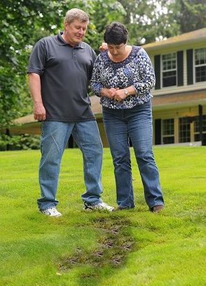 Homeowners standing over wet soggy yard from failing septic system